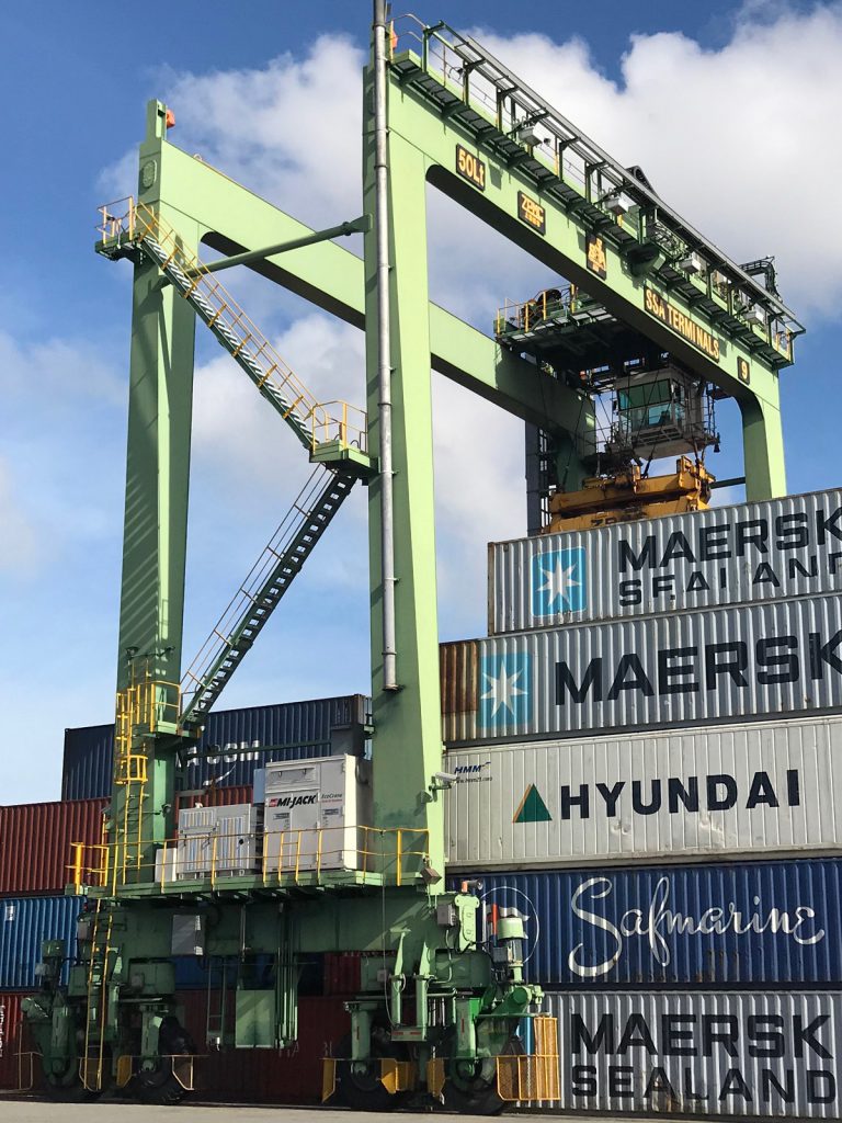 Photo shows hybrid rubber-tire gantry crane working a stack of containers on marine terminal using battery power